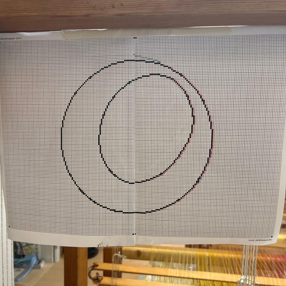 Carton mis au carreau suspendu au métier : double cercle reporté case par case sur papier quadrillé.