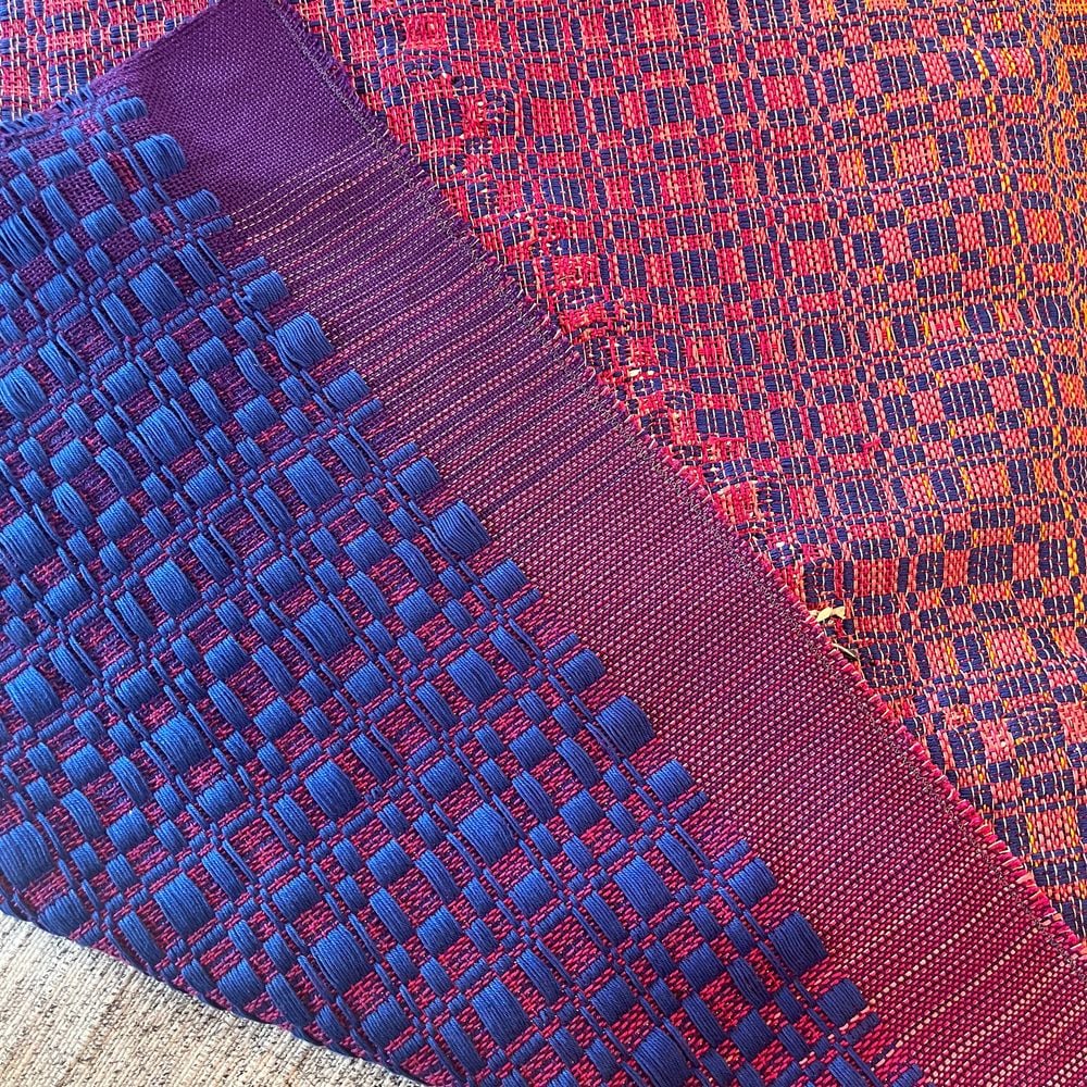 Le devant de la pièce, replié sur lui-même : armure Munkabälte rouge et bleue, bordure fuchsia tissée serrée.