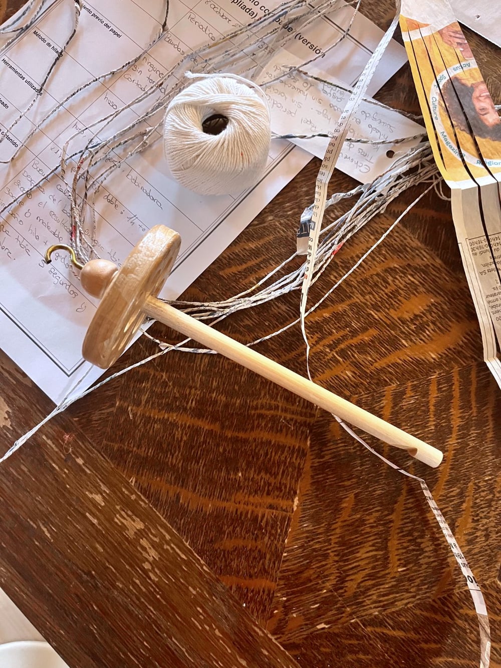Fuseau, fil de papier journal torsadé, et notes manuscrites en espagnol sur une table en bois