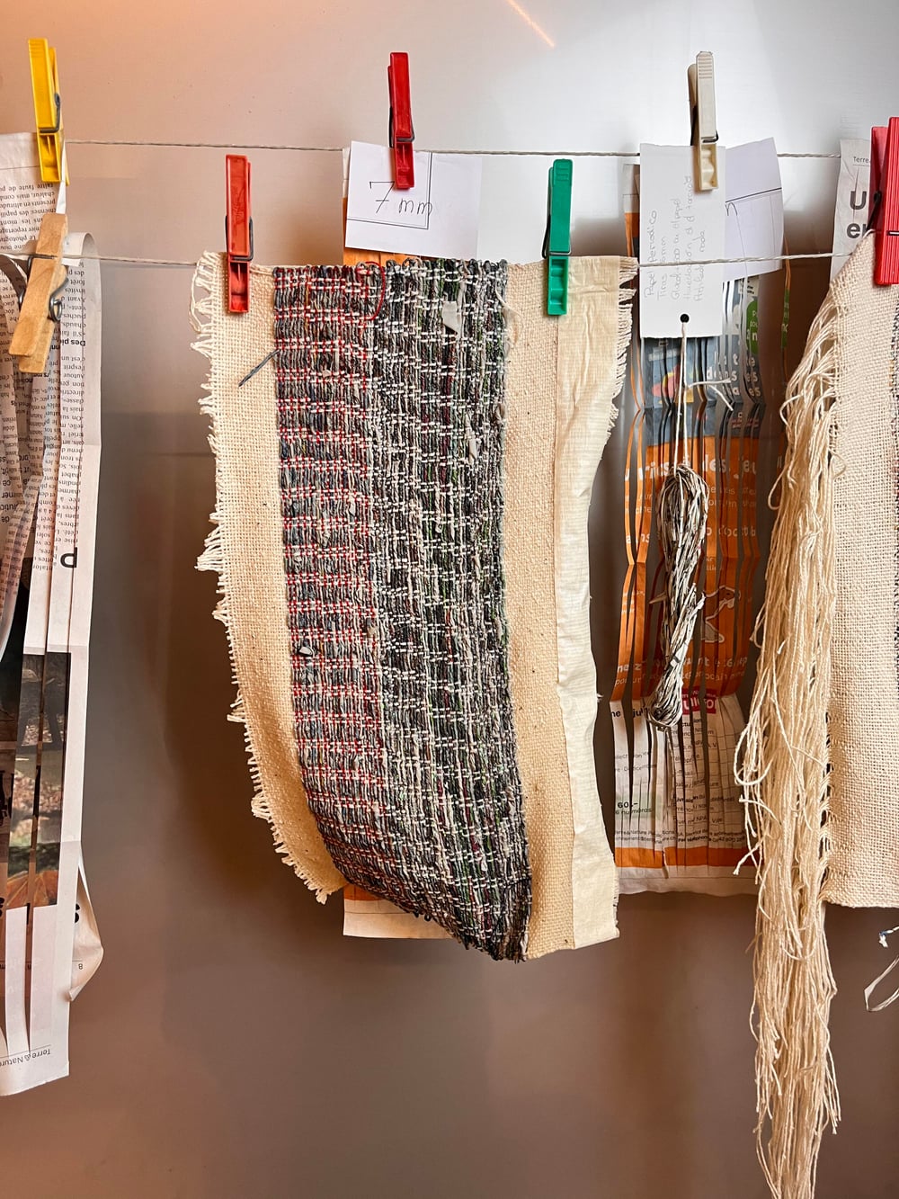 Échantillons papier journal et coton suspendus à un fil par des pinces à linge en bois, structures rustiques.