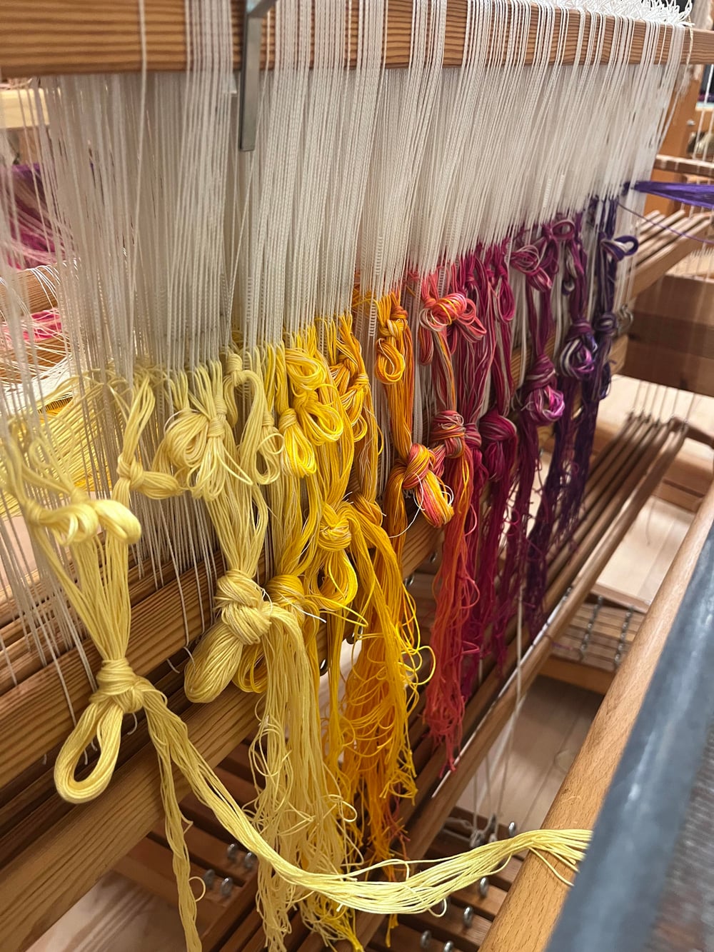 Écheveau de coton noué, dégradé continu du jaune à l’orange, magenta et violet profond.